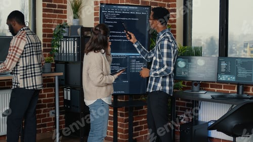 Preview: Team of database admins analyzing source code on wall screen tv comparing errors using tablet