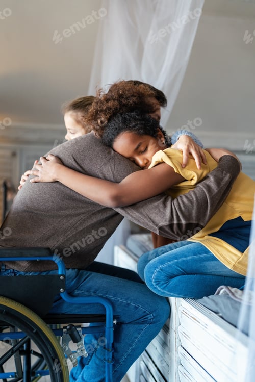 Preview: Portrait of happy loving father with disability in wheelchair hugging with multiethnic children