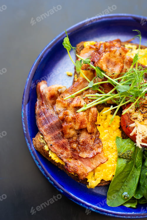 Preview: Very bright and healthy breakfast on a plate - bacon, egg, salad, tomato, cheese, a glass of yogurt.