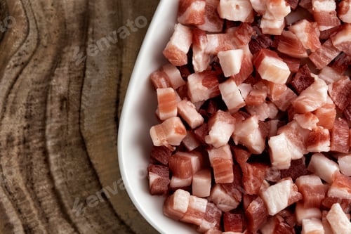 Preview: Italian pancetta, bacon cubes, diced ham, cutted pork in square white plate on wooden textured
