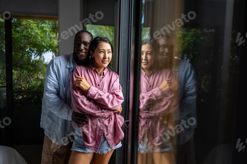 Preview: Young diverse couple joyfully smiling together in their bright living room, wearing casual clothes