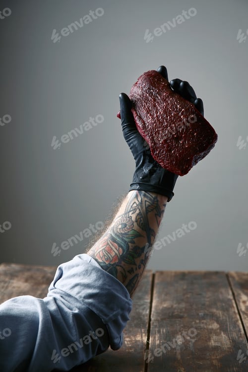 Preview: tattooed left hand black silicon glove holds fresh whale meat steak