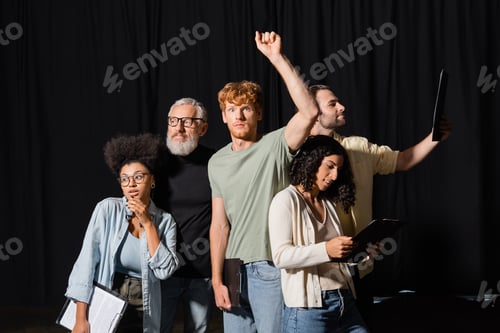 Preview: redhead man standing with raised hand near bearded art director and interracial actors with