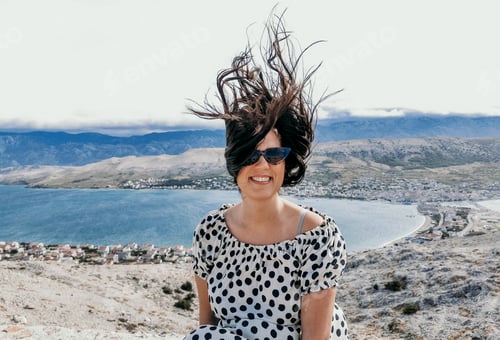Preview: Portrait of happy young woman on viewpoint above sea, hair blowing in the wind. Pag, Croatia.