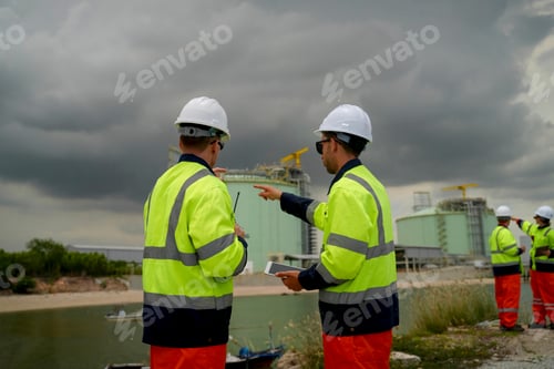 Preview: Engineers discuss project details near industrial site under overcast sky