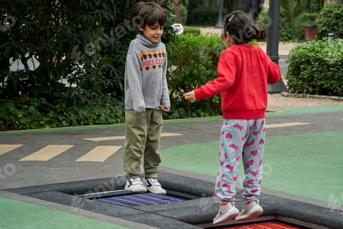 Preview: Happy boy and girl jumping together on trampoline
