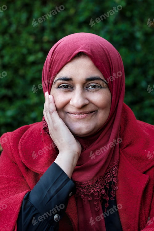 Preview: Muslim mature woman wearing hijab posing smiling in a red outfit.