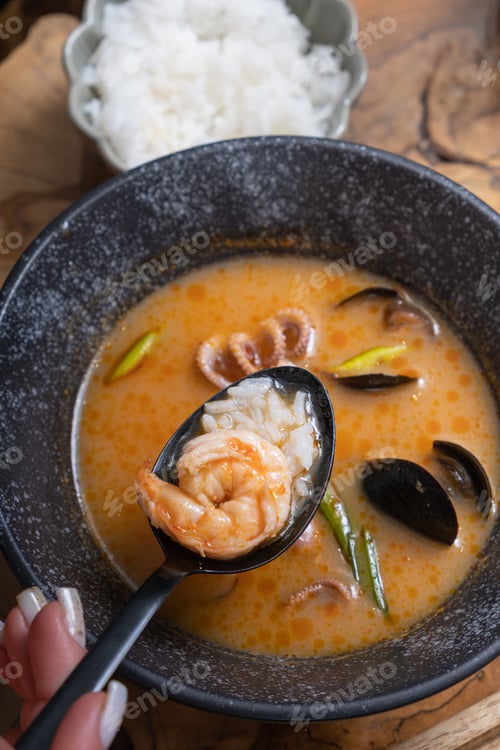 Preview: Close up shrimp and rice on spoon on the background of tom yum soup