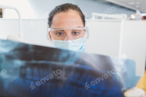 Preview: Dentist wearing surgical mask and safety glasses studying the x-ray