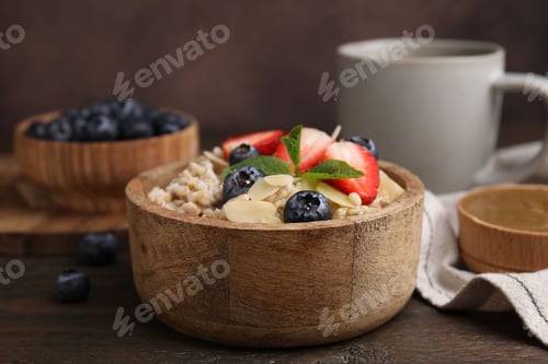 Preview: Tasty oatmeal with strawberries, blueberries and almond flakes in bowl on wooden table, closeup