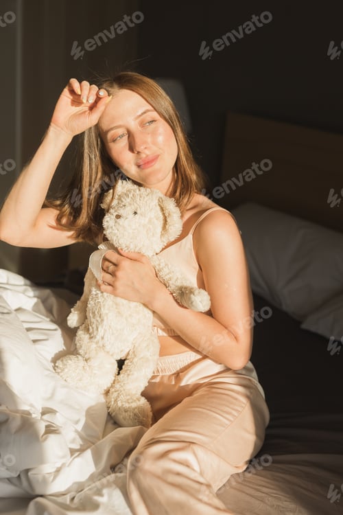 Preview: Girl is waking up in morning stretches in bed and sun shines from window. Happy young woman greets