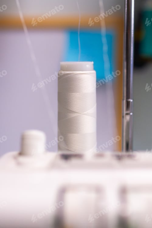 Preview: White thread spool on sewing machine with blurred background.