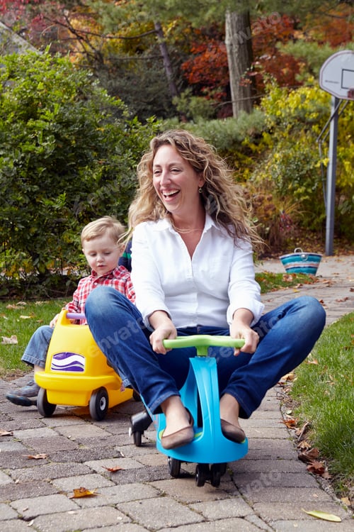 Preview: Mother and young son riding on toy cars in garden