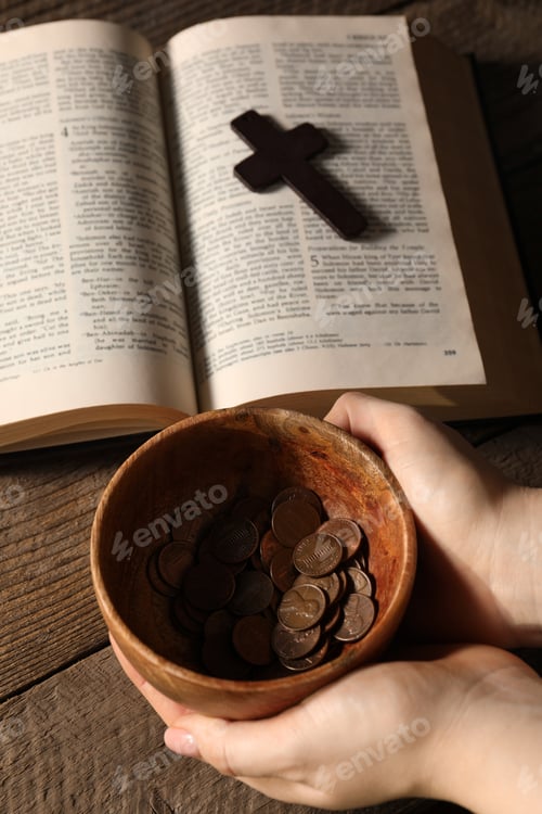 Preview: Donate and give concept. Woman holding bowl of coins, closeup. Bible and cross on wooden table