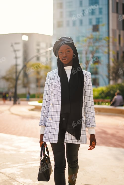 Preview: Trendy black woman in headscarf carrying bag in park