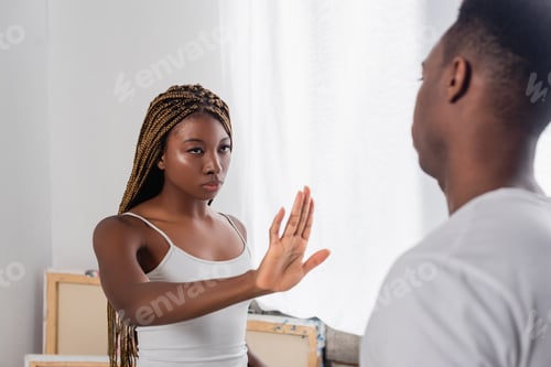 Preview: African american woman showing stop gesture near boyfriend on blurred foreground at home