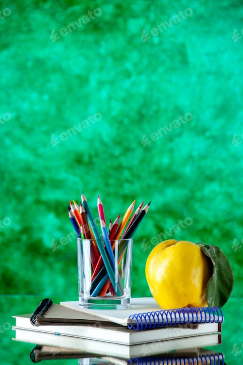 Preview: Vertical view of colored pencils kept in a glass jar and quince with stem on stacked spiral