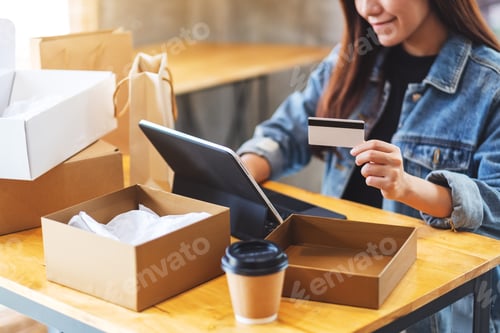 Preview: a young asian woman using tablet pc and credit card for online shopping with postal parcel box