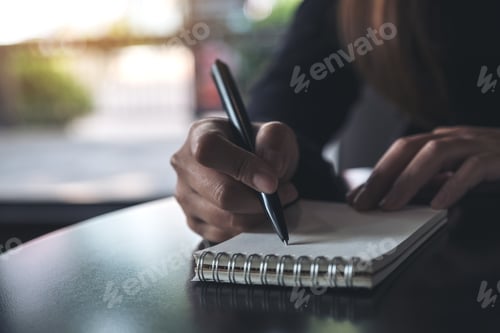 Preview: Closeup image of a woman's hands writing down on a white blank notebook on table