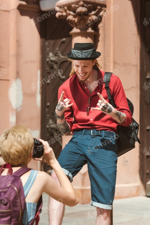 Preview: woman taking photo of boyfriend showing rock signs