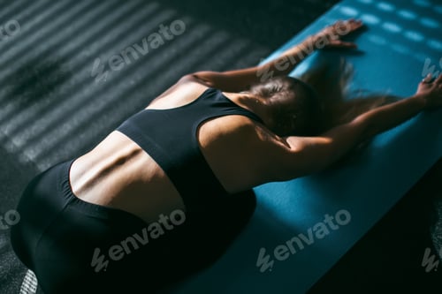 Preview: Beautiful young woman working out in gym, doing forward bend yoga exercise on blue mat, close-up