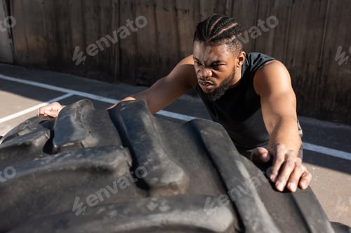 Preview: high angle view of sportive african american man training with tire on street