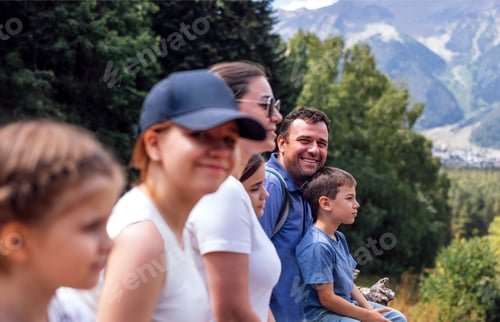 Preview: Happy family of tourists is sitting on log and enjoying mountain scenery. Back view