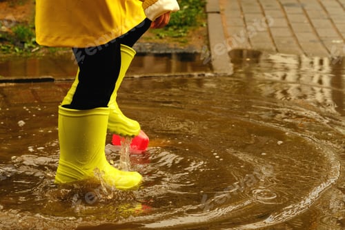 Preview: child jumps in a puddle arranges a storm for a small plastic boat. legs in yellow rubber boots.