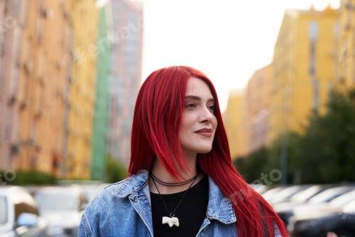 Preview: Young woman with vibrant red hair walks through urban street in summer