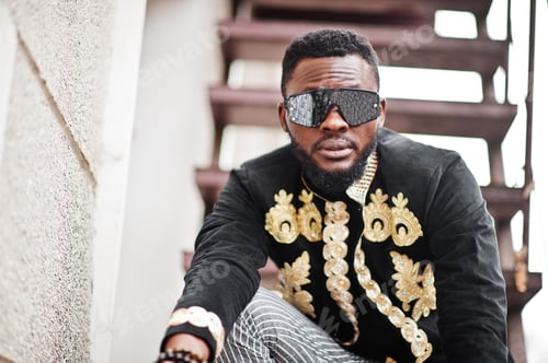 Preview: Mega stylish african man in traditional jacket pose. Fashionable black guy in hat and sunglasses.