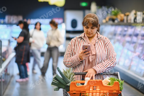 Preview: Indian woman using smartphone while shopping in grocery store
