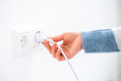 Hand Plugging White Power Cord into Electrical Outlet