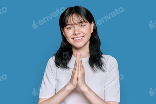 Preview: Young female pleading, holding hands in prayer on blue background