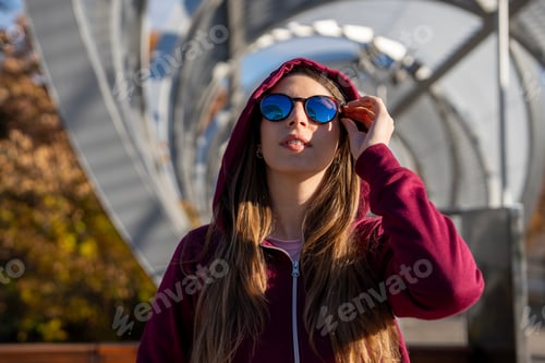 Preview: Young woman wearing sunglasses and hoodie in urban setting