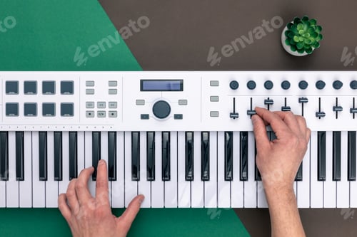 Preview: Hands of a man playing musical keys on a colored background, flat lay.
