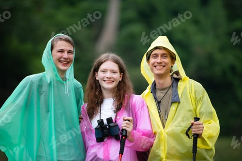 Preview: Group of happy friends in raincoats and raincoats looking at mountain and forest
