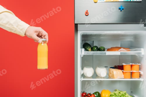 Preview: cropped view of man holding bottle of juice near open fridge with fresh food on shelves isolated on