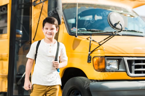 Preview: happy little pupil with backpack standing in front of school bus