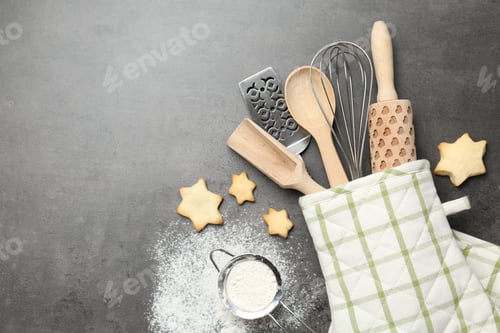 Preview: Different kitchen utensils in oven mitten, flour and cookies on grey table, flat lay. Space for text