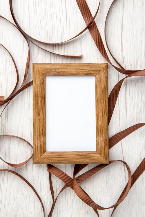 Preview: Vertical view of small brown empty wooden picture frame around ribbon on white background