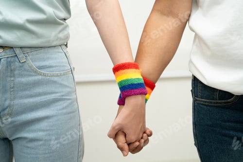 Preview: Asian LGBT couple woman holding hand wearing rainbow wristband.