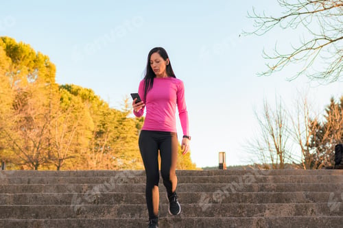 Preview: Sporty woman looks at a mobile phone in a park at sunset