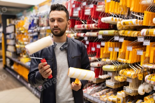 Preview: a man in a construction store picks up a roller for acrylic and oil paint next to a rack with tools