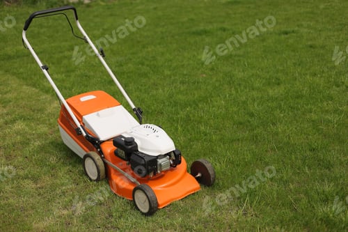 Preview: Top view of modern orange-grey electric lawn mower cutting bright lush green grass. Gardening work