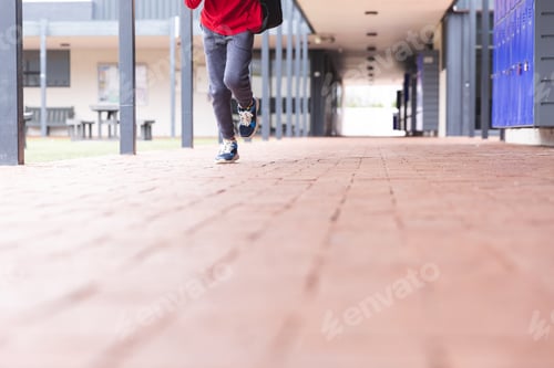 Preview: In school, young biracial male student is running along a corridor outdoors with copy space