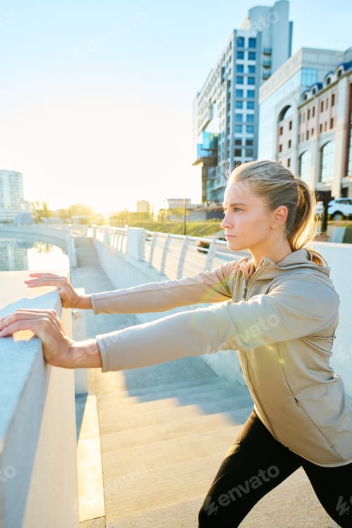 Preview: Young sportswoman in grey sport jacket keeping arms stretched during exercise
