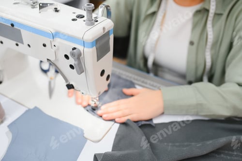 Preview: Young dressmaker woman sews clothes on working table.