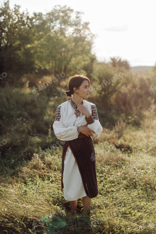 Preview: Young woman in traditional national embroidered shirt and skirt on nature at sunset.