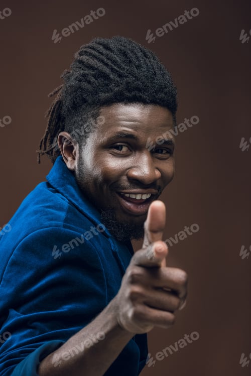 Preview: smiling african american man pointing on camera isolated on brown