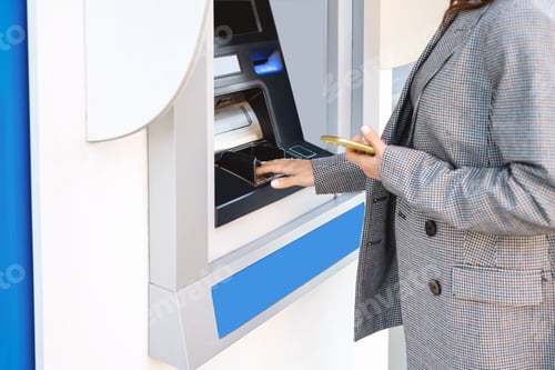 Preview: Businesswoman in a smart casual outfit using an ATM on a city street.